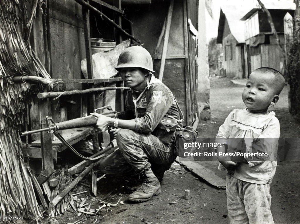 War and Conflict The Vietnam War. pic: 1968. South Vietnam. A fearless youngster oblivious to danger stands alongside a crouching South Vietnamese soldier in a village street.