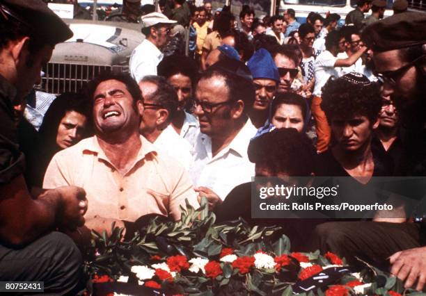 Mourners crowding around members of the Israel Defense Forces seated in the rear of military trucks, each containing a flower covered coffin of one...