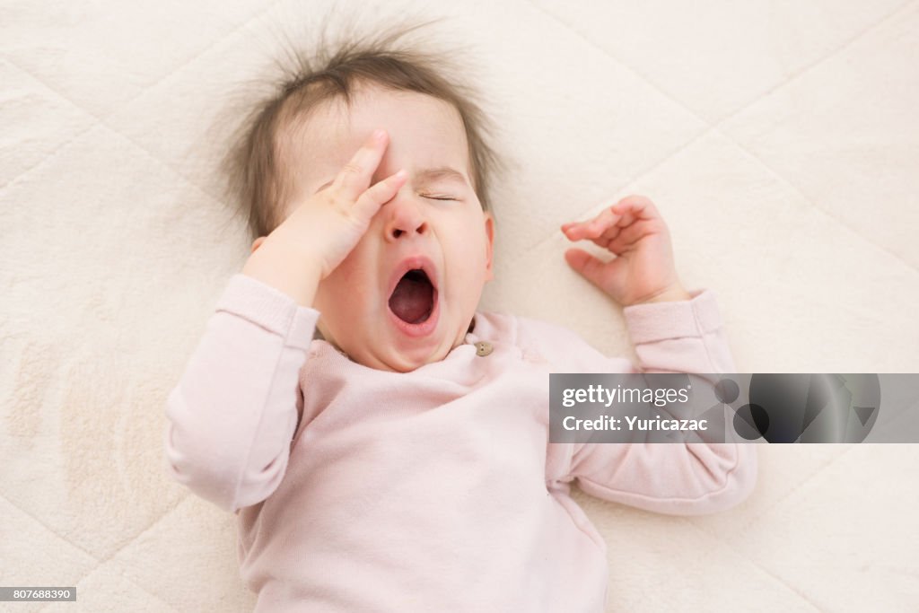 Portrait of sleeping beautiful and yawning baby toddler on the bed wearing pink pullover. Bedtime. Nursery