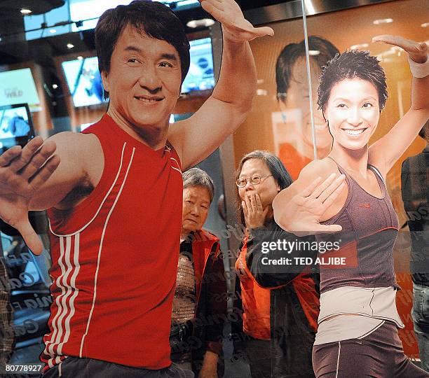 Two elderly women watch customers next to a giant poster of Hong kong action star Jackie Chan during the opening ceremony of a fitness center in Hong...