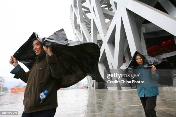 Spectators cover themselves with plastic as they leave the National Stadium to watch the "Good Luck Beijing" 2008 Beijing International Marathon Race...