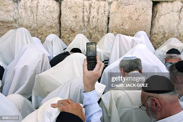 Man uses his mobile phone to make a video call as Jewish priests or Cohanim cover their heads and faces with the their Talit, or prayer shawl, as...