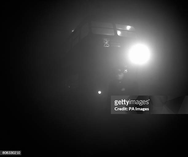 London Transport inspector holding a flare leads a bus out of the terminus at Aldgate East as dense fog again blanketed London, causing widespread...