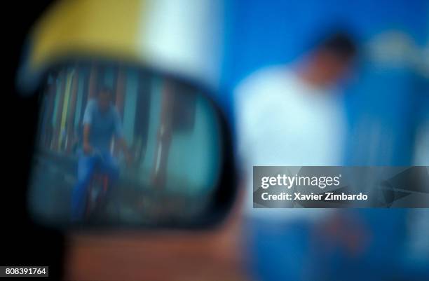 Silhouette of a man seen through a car window and man riding a bicycle seen in a outside rear-view mirror in a colourful street on May 17, 2001 at...