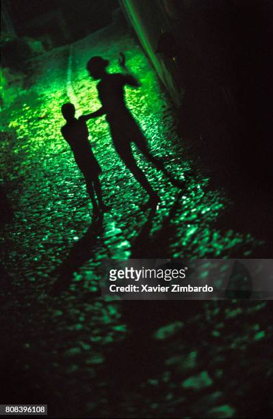 Silhouettes of a young woman dancing and a young boy standing still at night with green light in a cobblestone street on May 11, 2001 at Trinidad,...