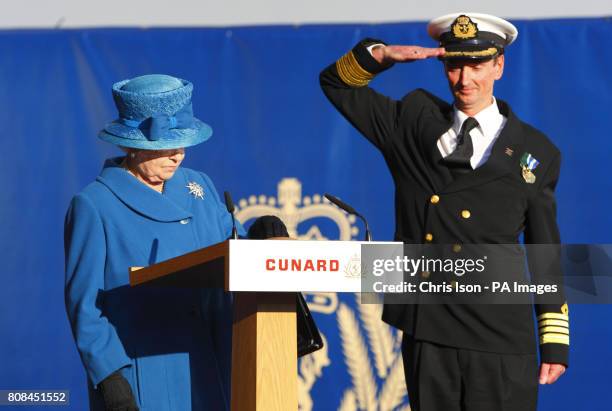 Christopher Wells, Captain of the Queen Elizabeth, salutes as Her Majesty Queen Elizabeth II presses a button to release the bottle of white wine to...