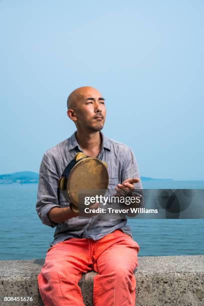 man sitting by the sea playing a percussion instrument - 剃った頭 ストックフォトと画像