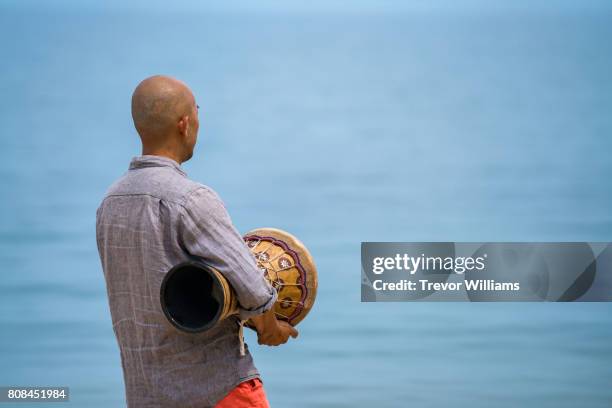 man facing the ocean while holding and playing percussion instruments - drum top view stock-fotos und bilder