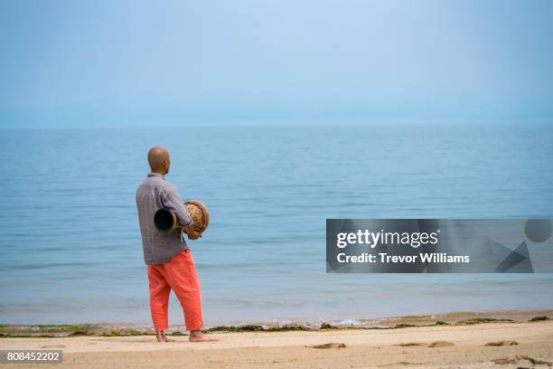 man facing the ocean while holding and playing percussion instruments - drum top view stock-fotos und bilder