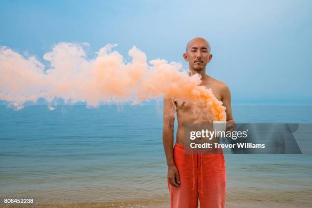 man holding a smoldering cup with smoke blowing down the beach - halbbekleidet stock-fotos und bilder