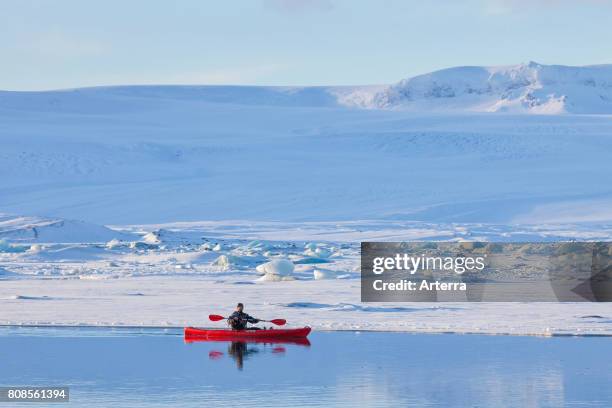 Kayaker in red kayak on the Jkulsrln glacier lagoon in winter, glacial lake in southeast Iceland.