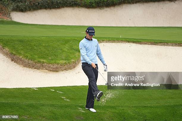 Justin Rose of England cleans the sand off his shoes upon exiting a greenside bunker on the 12th hole during the second day of practice prior to the...