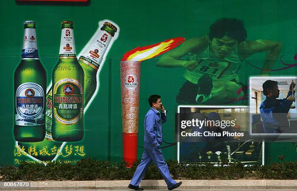 Worker walks past a billboard featuring beer and Olympic Torch at the Tsingtao Beer Factory, China's biggest beer brewery and the Official Domestic...