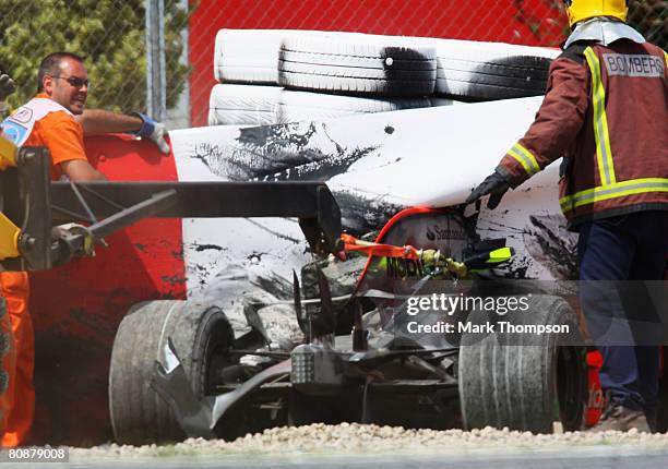 Rescue workers try to retrieve the crashed car of Heikki Kovalainen of Finland and McLaren Mercedes as he sits imbedded in the safety barriers after...