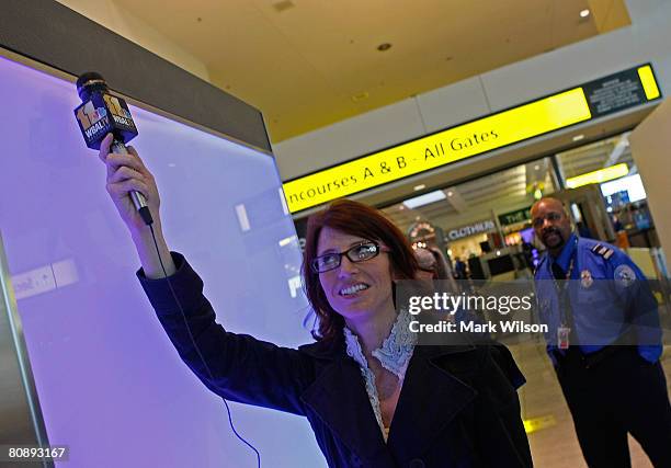 Reporter Kate Amara holds her microphone up to a speaker to hear soft music playing for travelers passing through a new and improved security check...