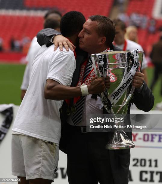 Swansea City's Scott Sinclair hugs manager Brendan Rodgers whilst holding the Championship Play Off trophy.