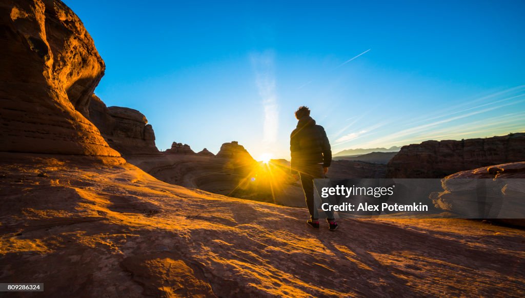 Il giovane hipster, viaggiatore ed escursionista, ammirando l'alba nel canyon rosso vicino a Delicate Arch, nello Utah, all'alba