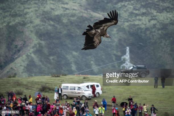 This picture taken on May 29, 2017 shows a vulture flying near ethnic Tibetans and Chinese tourists gathering for a sky burial near the partially...