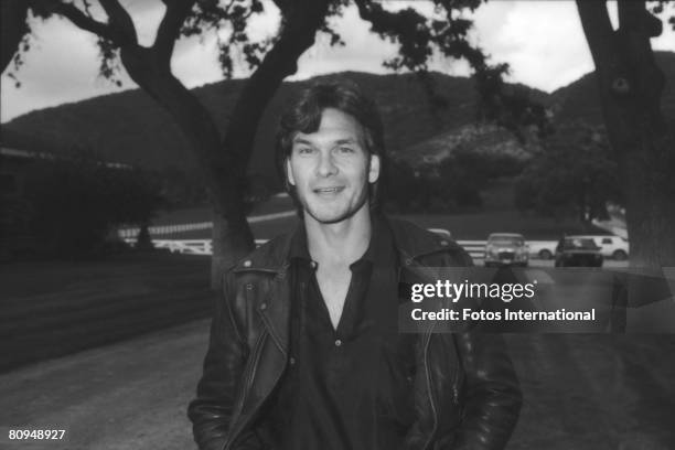 American actor Patrick Swayze smiles as he poses in a leather jacket at a charity auction of Arabian horses for AIDS research on the grounds of...