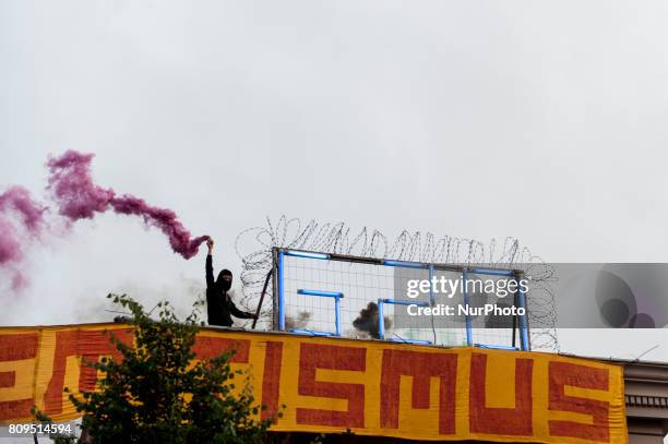 Woman holds a smoke grenade beside a G20 neon sign on the roof of the autonomous center Rote Flora in the air. About 20000 people demonstrated in a...