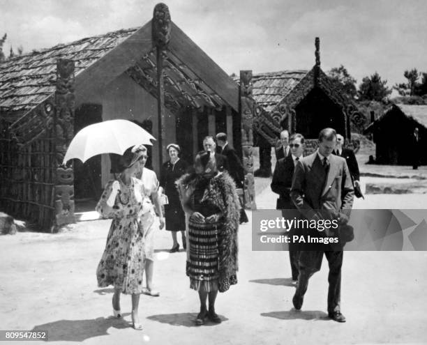 **Scanned low-res from contact** The Queen, sheltering beneath a sunshade, talks with Maori guide Rangi as she leaves the Meeting House during the...