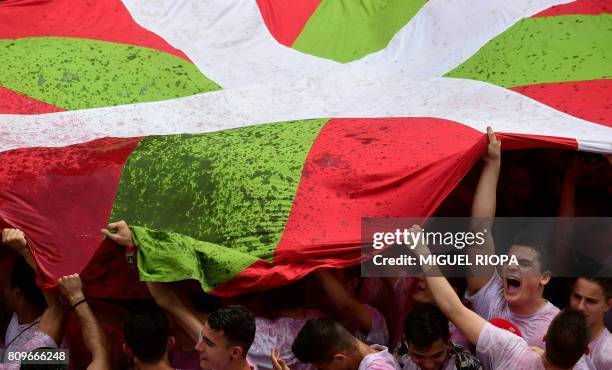 Revellers hold up a big "Ikurrina" as they celebrate the 'Chupinazo' to mark the kickoff at noon sharp of the San Fermin Festival, in front of the...