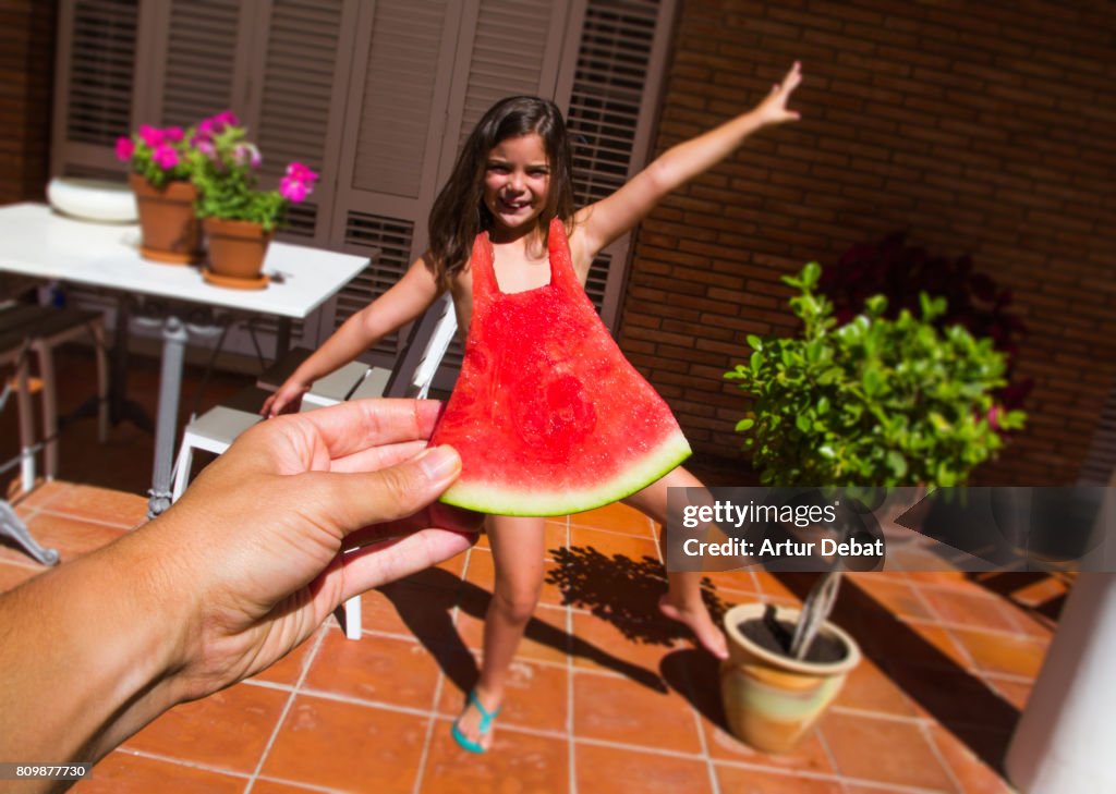 Funny picture of a watermelon dress challenge taken from personal point of view fitting a size of watermelon with a little girl, playing with perspective.