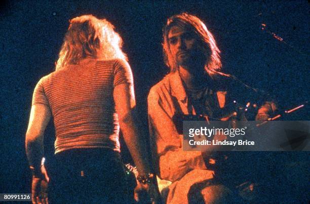 September 8: Kurt Cobain, a symbolic Band-Aid on his forehead, seated onstage with acoustic guitar, looks into the distance as Courtney Love passes...