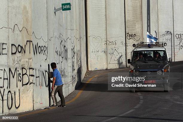 Palestinian boy waits for an Israeli police patrol to pass by before playing soccer under Israel's separation barrier May 4, 2008 where the...