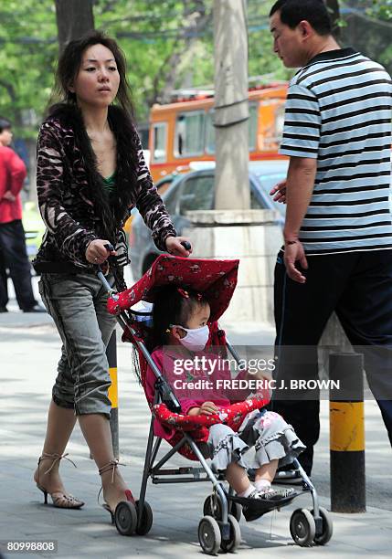 Woman pushes a stroller with as a child wears a face mask near a children's hospital in Beijing on May 6, 2008. Ten doctors and officials in China...