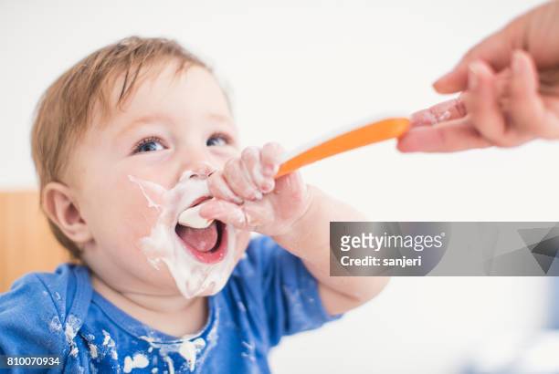onherkenbaar persoon yoghurt met een lepel te geven aan een jongetje - baby eating yogurt stockfoto's en -beelden