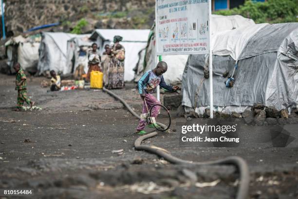 Boy walks on a water pipe while rolling a hoop in Lac Vert IDP camp on June 24, 2014 in Mugunga, Democratic Republic of Congo. Congolese in the North...