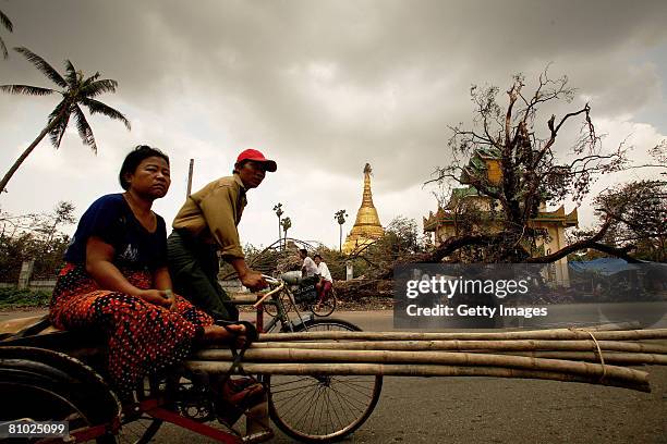 People ride a bike past an uprooted tree on May 8, 2008 in downtown Yangon, Myanmar. It has been estimated that more than 100,000 people were killed...