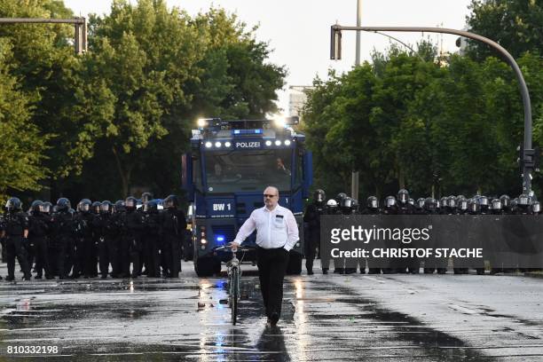 Man wheels his bicycle in front of riot police with water cannon during a protest on July 7, 2017 in Hamburg, northern Germany, where leaders of the...