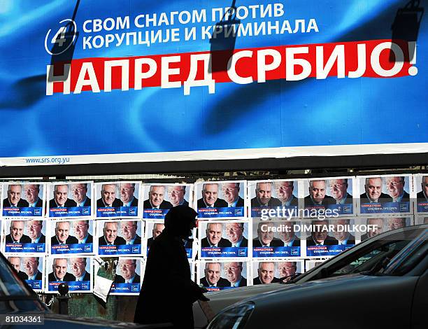 An elderly woman begs by pre-election posters of Vojislav Seselj, currently on trial in The Hague for war crimes, leader of the hard-line nationalist...