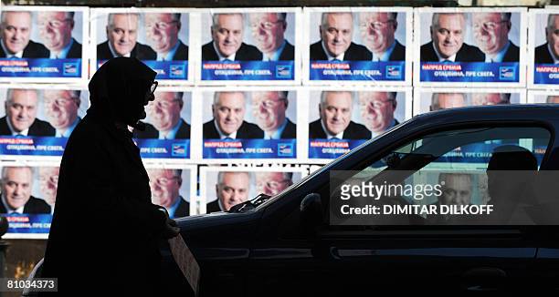 An elderly woman begs for money at a traffic jam by pre-election posters of Vojislav Seselj, currently on trial in The Hague for war crimes, leader...