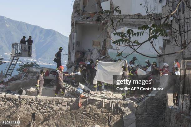 Firefighters block the view with sheets as they extract a body from the debris of a collapsed building, after two floors collapsed in a small...