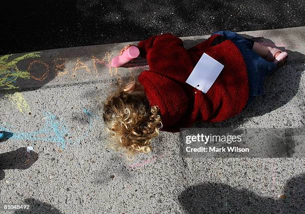 Lucy Brown plays with sidewalk chalk while sitting with her mother while Democratic presidential hopeful Sen. Barack Obama speaks to reporters after...