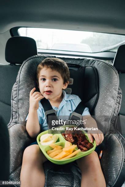 boy sitting in car seat eating breakfast - toddler in car foto e immagini stock
