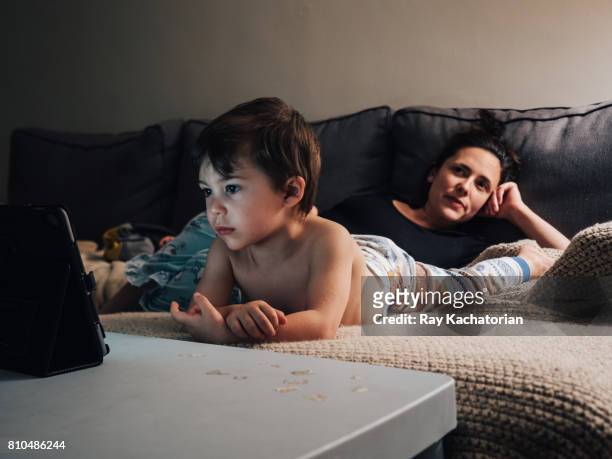 child watching tablet mother looking off - boy in pajamas and mom on tablet stock-fotos und bilder