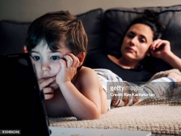 child watching tablet mother looking at child - boy in pajamas and mom on tablet stock-fotos und bilder