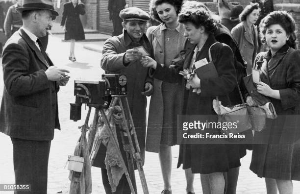 Street photographer shows some of his work to clients, London, 27th March 1946. The photographer is using a 1930's Aptus ferrotype camera with a...
