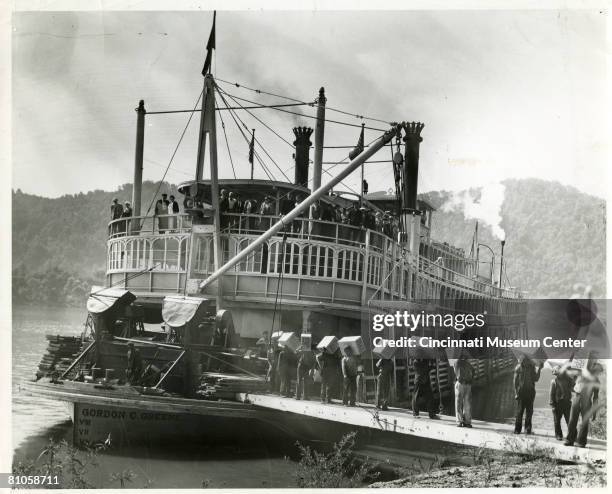 Passengers and crew stand at the railing of the 'cabin deck' of the paddle steamer 'Gordon C. Greene' as roustabouts unload boxes of 'Clean Quick...