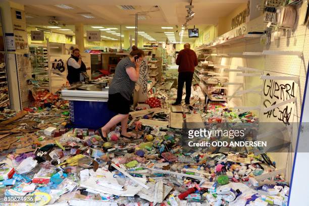 Woman uses her mobile phone as she stands in a looted Budnikowsky drugstore in Hamburg's Schanzenviertel district on July 8, 2017 in Hamburg,...