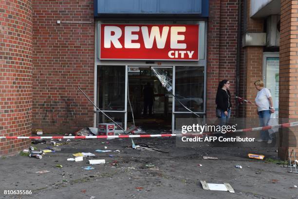 Two women stand in front of a destroyed Rewe City supermarket after riots in Hamburg's Schanzenviertel district on July 8, 2017 in Hamburg, northern...