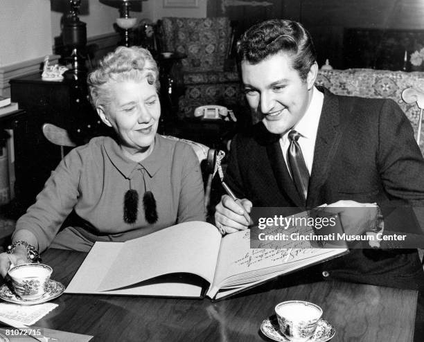 American radio and television broadcaster Ruth Lyons smiles as she watches popular American painist Liberace sign the guest book for her influential...