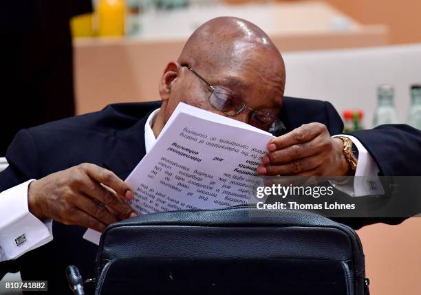 South African President Jacob Zuma talks on a mobile phone while at the same time looking through documents from his briefcase at the morning working...