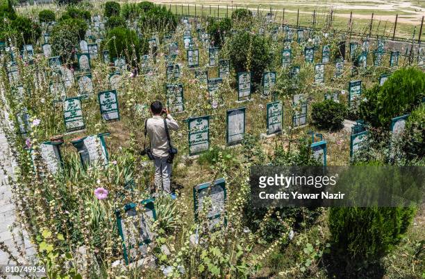 Photographer takes pictures of headstones on the graves at the martyrs graveyard during a curfew, on the the first death anniversary of Burhan Wani a...