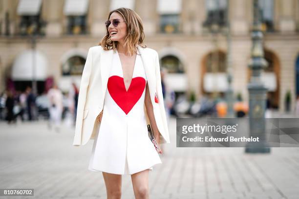 Olivia Palermo wears a white blazer jacket, a white low neck dress with a printed red heart, a clutch, black and white shoes, at Place Vendome,...