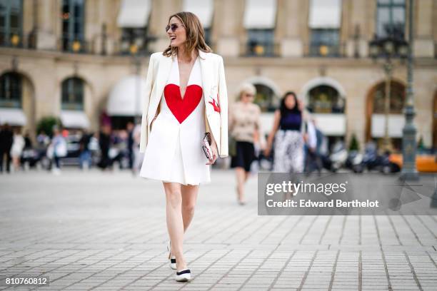 Olivia Palermo wears a white blazer jacket, a white low neck dress with a printed red heart, a clutch, black and white shoes, at Place Vendome,...